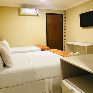 a hotel room with two beds and a television at Hotel Pousada Latitude in Canoa Quebrada