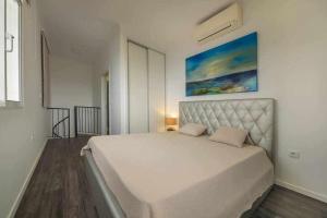 ein Schlafzimmer mit einem großen weißen Bett mit einem Gemälde an der Wand in der Unterkunft Lombo do Doutor Cottage 1 by Mth in Calheta