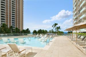 a swimming pool with lounge chairs and the ocean at Ilikai Lite in Honolulu