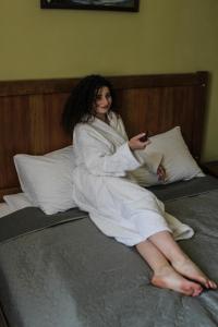 a woman sitting on a bed holding a cell phone at Sadyba DarKa in Ternopil