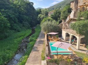 ein Schwimmbad mit einem Regenschirm neben einem Fluss in der Unterkunft Les Terrasses, gîtes en Cévennes in Saint-Jean-de-Valériscle