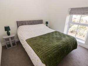 a bedroom with a bed with a green blanket and a window at Golygfa Bryn in Porth