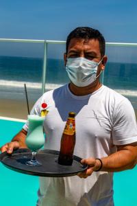 un uomo che tiene un drink e una bottiglia su un vassoio di Hotel Del Mar Mancora a Máncora