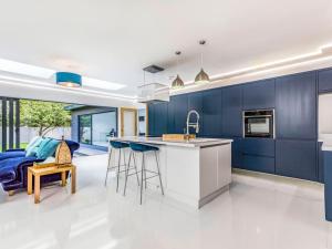 a kitchen with blue cabinets and a bar with stools at Luxury West Sussex Seaside Family Retreat in Bognor Regis