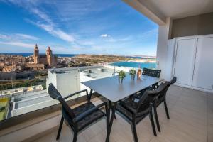 a table and chairs on a balcony with a view of the city at Clifftop Modern Apartment in Mellieħa