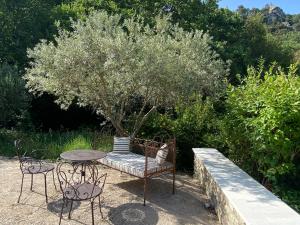 un chat assis sur un banc à côté d'une table et d'un arbre dans l'établissement Aux Dentelles, à La Roque-Alric