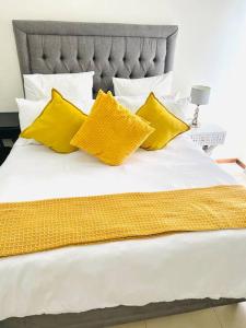 a white bed with yellow pillows and a gray headboard at 1 Bed Apartment @ Jackal Creek Golf Estate in Roodepoort