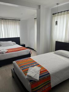 two beds in a bedroom with white walls and windows at Hostal Entre Ríos in Cuenca