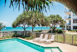 a swimming pool with lounge chairs and the ocean at Pandanus Court in Caloundra