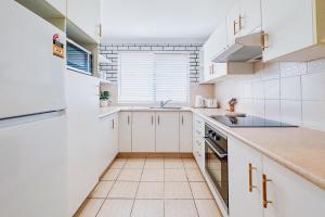 a white kitchen with white cabinets and a sink at Seaside Haven, 3-62 Tomaree Rd - Wi-Fi and perfect for families in Shoal Bay +14 photos
