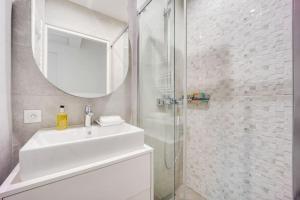 La salle de bains blanche est pourvue d'un lavabo et d'un miroir. dans l'établissement Luxueux appartement au cœur de Neuilly - Proche Paris, à Neuilly-sur-Seine