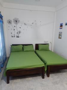 two beds in a room with green sheets at Beach Guest House Addalaichenai in Addalachenai