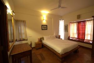 a bedroom with a bed and a table and windows at Nisargha Serviced Apartments in Bangalore