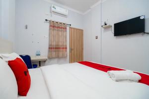 um quarto com uma cama branca com almofadas vermelhas e uma televisão em RedDoorz at Homestay Lotus 2 Pangkal Pinang em Pangkalpinang