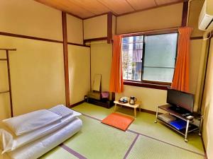 1 dormitorio con 1 cama, TV y ventana en Yamamoto Ryokan, en Fukuoka
