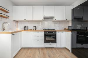 a white kitchen with wooden floors and white cabinets at Apartment Near the Warta River by Renters in Poznań