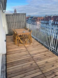 eine Holzterrasse mit einem Holztisch auf dem Balkon in der Unterkunft Le Brasilia - Appartement neuf pour 4 personnes avec terrasse in Straßburg