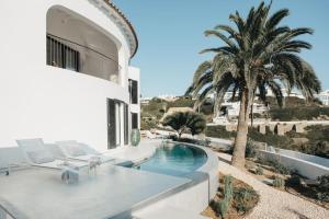 a white house with a swimming pool and palm trees at Villa Alma luxe & sea views in Cala Llonga