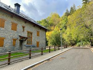 a stone building with a wooden fence next to a road at Àtic de luxe i rústic a Esterri d'Àneu by RURAL D'ÀNEU in Esterri d'Àneu