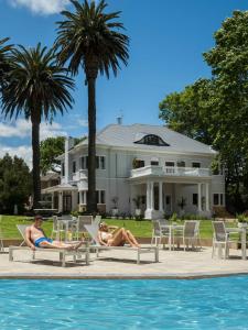 two people laying on chairs by a pool in front of a house at Palm House Boutique Hotel in Cape Town