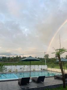 un arco iris sobre una piscina con sillas y sombrilla en Pondok Tetebatu Cottages and Cafe, en Tetebatu