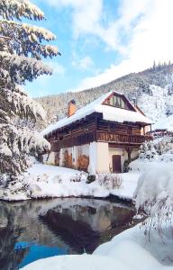 a house covered in snow next to a river at Drevenica Inga in Staré Hory
