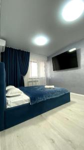 a bedroom with a blue bed and a flat screen tv at Евродвушка в ЖК Каратал in Kostanay