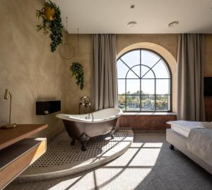 a bathroom with a tub and a bed and a window at Bordűr Wellness Hotel Superior és Szőnyegmúzeum in Békésszentandrás