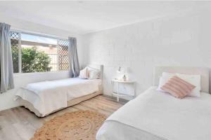a white bedroom with two beds and a window at Island Villas - Lady Musgrave - Unit 1 in Bundaberg