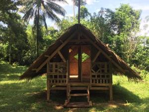 a small hut with a thatched roof in the grass at Pandora Glamping in Quezon