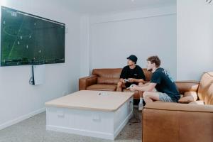 deux hommes assis dans un salon jouant à un jeu vidéo dans l'établissement Surf Inn Boutique Backpackers - FREE BREAKFAST, à Gold Coast