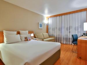 um quarto de hotel com uma grande cama branca e uma secretária em Novotel RJ Santos Dumont no Rio de Janeiro