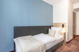 - une chambre avec un lit blanc et un mur bleu dans l'établissement theAmbassador Hotel I Essen City, à Essen