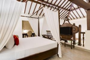 1 dormitorio con 1 cama con cortinas y TV en Lemon Tree Amarante Beach Resort, Goa, en Candolim