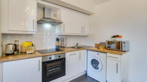 a kitchen with white cabinets and a washer and dryer at Daffodil Cottage in Penclawdd