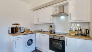 a kitchen with white cabinets and a washer and dryer at Bluebell Cottage in Penclawdd