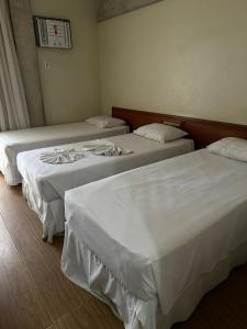 two beds in a hotel room with white sheets at Hotel Sol da Praia in Vitória
