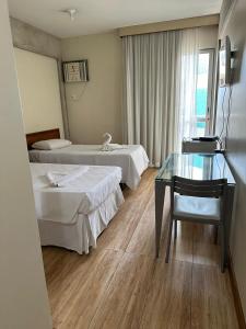 a hotel room with two beds and a glass table at Hotel Sol da Praia in Vitória