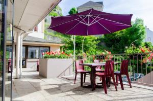 a table and chairs with a purple umbrella on a patio at Hôtel Hélianthe in Lourdes