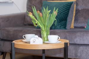 a table with two cups and a vase with flowers on it at Apartament EMELIE Dziwnówek nad morzem EPapartamenty in Dziwnówek