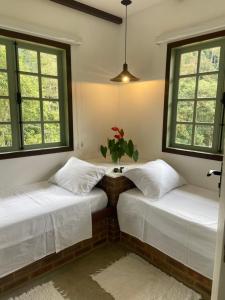 two beds in a room with two windows at Matha Pousada e Bistrô in Lumiar