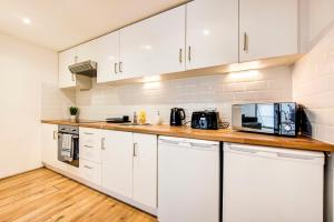 a kitchen with white cabinets and a wooden counter top at That Cosy Stay - Fantastic 2 Bed Apartment - Stratford in London