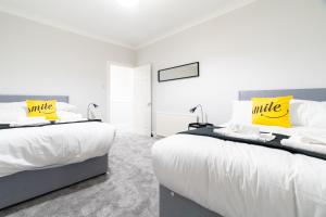 two beds in a bedroom with white and yellow pillows at Bell Apartment in Airdrie