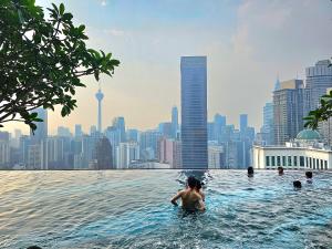 a person in a infinity pool with a city skyline at The Axon Residence Bukit Bintang in Kuala Lumpur
