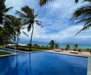 a swimming pool with palm trees and the ocean at Casa da Gameleira in Baía Formosa