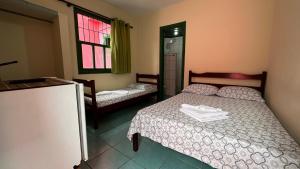 a bedroom with two beds and a refrigerator and a window at Suítes Casa Rosada in Ubatuba