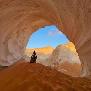 een vrouw die voor een boog in een woestijn zit bij White desert & Black desert camb in Qasr Al Farafirah