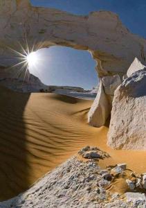 a desert with the sun shining through an arch in the sand at White desert & Black desert camb in Qasr Al Farafirah
