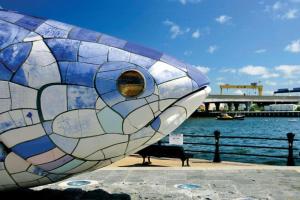 una escultura de vidrieras de pescado sentada junto a un banco en Central Haven en Belfast