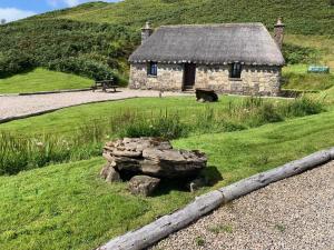 a stone building with a roof on a green field at Tigh Mairi at Mary's Thatched Cottages in Elgol